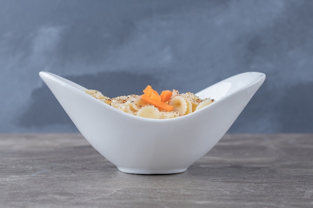 Toothsome farfalle pasta with spicy tomato sauce in bowl, on the marble.