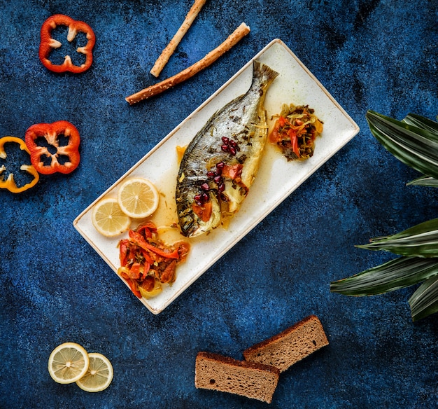 Free photo top  baked sea bass serves with vegetables and lemon on platter on blue