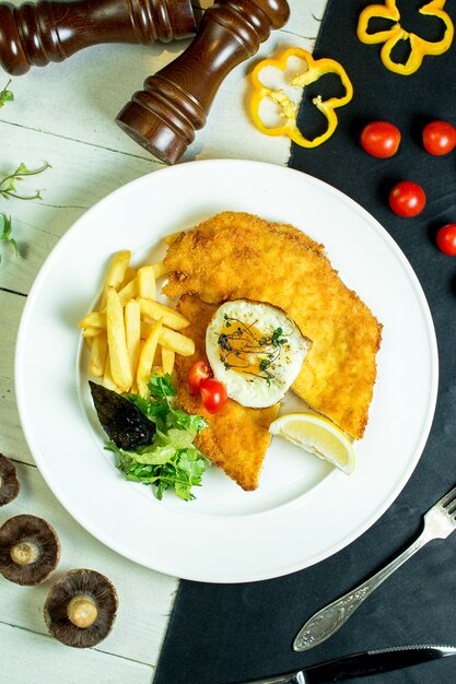 top  breaded chicken fillet served with french fries fried egg and cherry tomatoes on plate