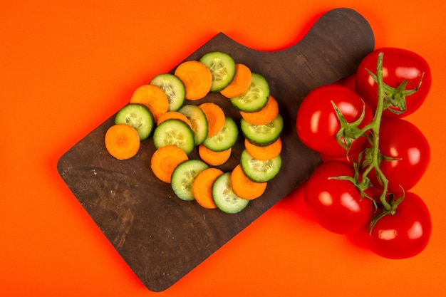 top  carrot and cucumber slices with tomatoes on wooden cutting board on orange