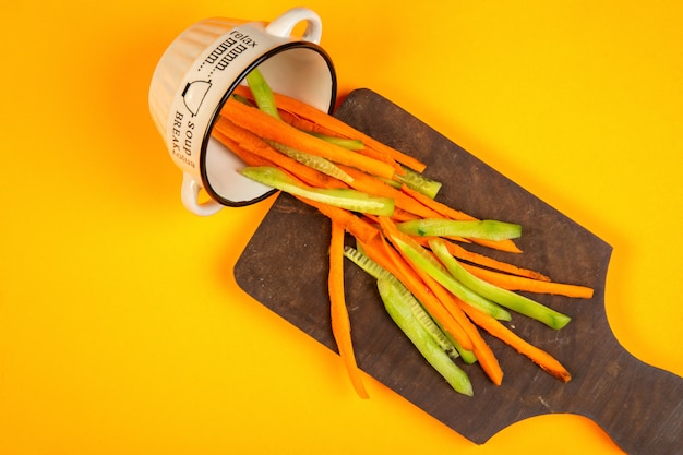 top  carrot and cucumber sticks on wooden cutting board on yellow