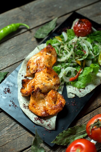 top  chicken kebab served with onions fresh herbs grilled tomato and pepper on black board