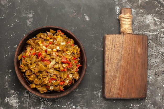 Free photo top close-up view appetizing dish an appetizing dish of green beans and tomatoes next to the wooden cutting board on the dark table