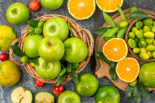 Top close-up view apples citrus fruits on the board apples with leaves in the basket cherries