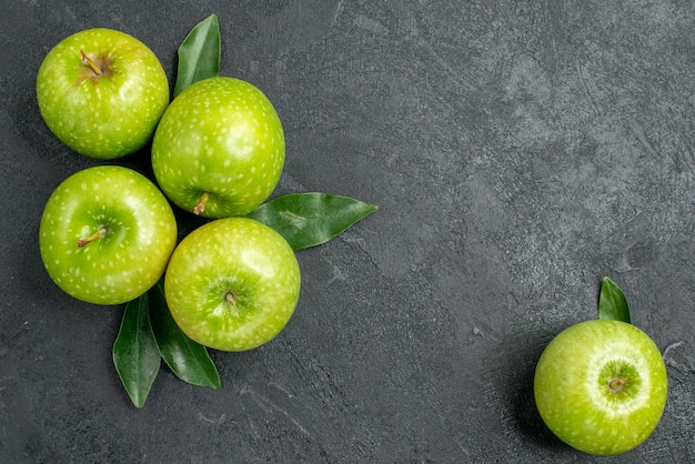 Free photo top close-up view apples four green apples with leaves next to the apple on the dark table