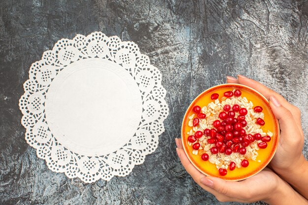 Free Photo top close-up view berries bowl of pomegranate seeds oatmeal in the hands lace doily