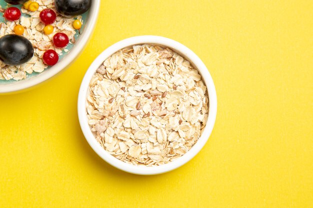 Top close-up view berries bowls of the appetizing oatmeal on the yellow table