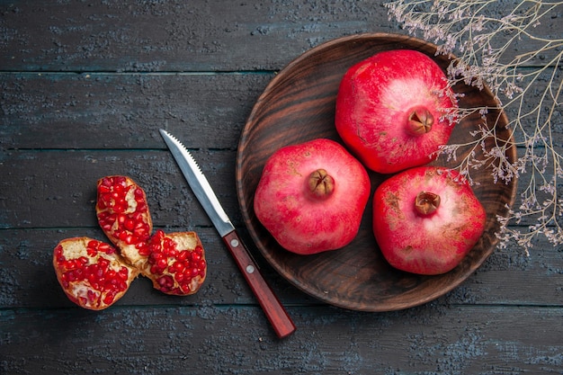 Top close-up view bowl of pomegranates bowl of pomegranates next to knife pilled pomegranate and tree branches