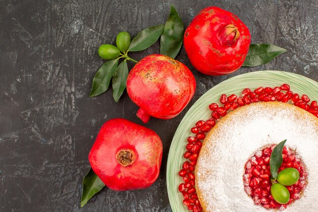 Top close-up view cake with pomegranate a plate of cake with pomegranate and three pomegranates