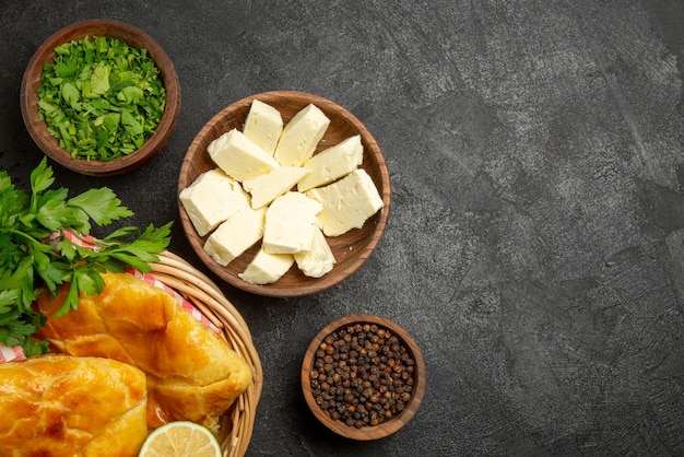 Top close-up view cheese herbs bowls of black pepper herbs and cheese and basket of an appetizing pies lemon herbs and checkered tablecloth on the table