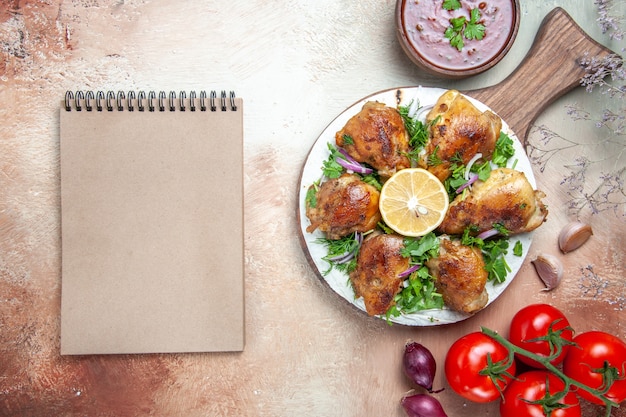 Top close-up view chicken chicken with herbs lemon on the board tomatoes sauce cream notebook