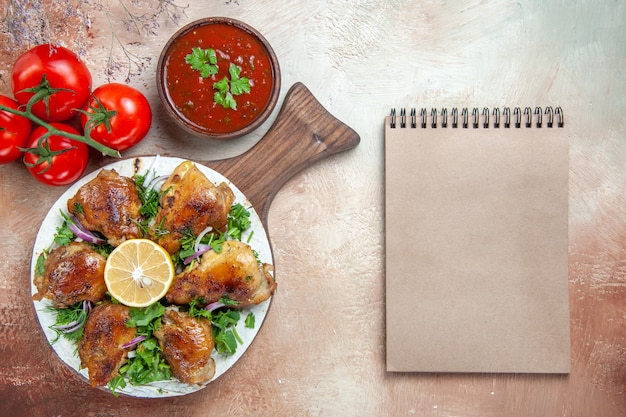 Free Photo top close-up view chicken sauce tomatoes chicken with lemon herbs on the board cream notebook