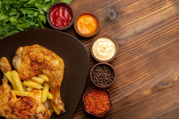 Top close-up view chicken and spices appetizing chicken legs french fries next to the herbs bowls of different sauces and spices