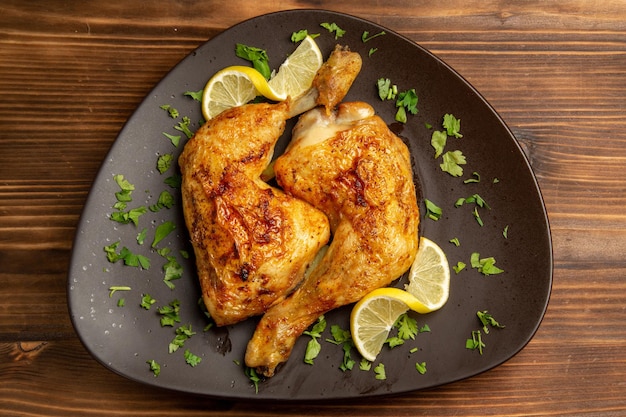 Top close-up view chicken with herbs chicken legs with herbs and lemon in the brown plate in the center of the table