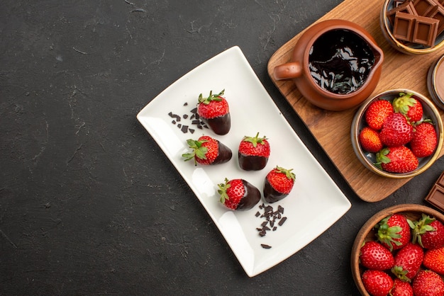 Free Photo top close-up view chocolate on board bars of chocolate next to the cutting board with chocolate cream and strawberries and chocolate-covered strawberries on plate