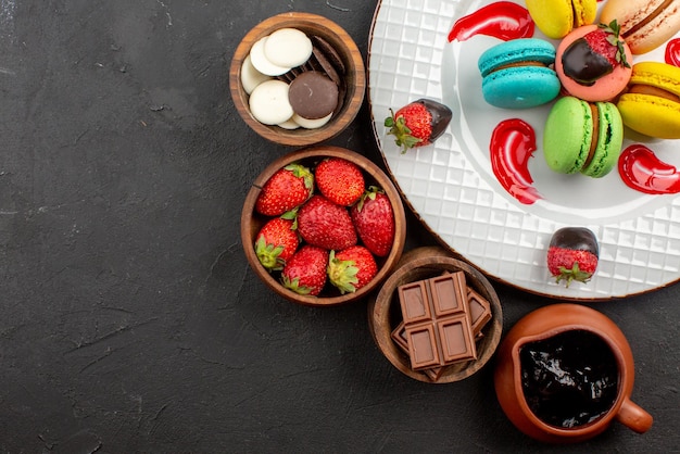 Top close-up view chocolate four bowls of chocolate strawberries and chocolate cream next to the plate of French macaroons and strawberries on the table