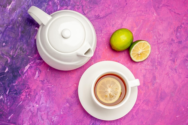 Free photo top close-up view a cup of tea white teapot a cup of black tea and limes on the pink table