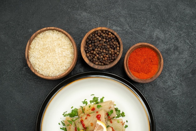 Free Photo top close-up view dish with spices appetizing stuffed cabbage with herbs lemon and sauce and bowls of colorful spices rice and black pepper on dark surface