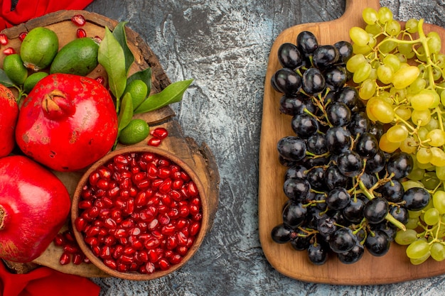 Top close-up view fruits bunches of grapes on the board pomegranates on the red tablecloth