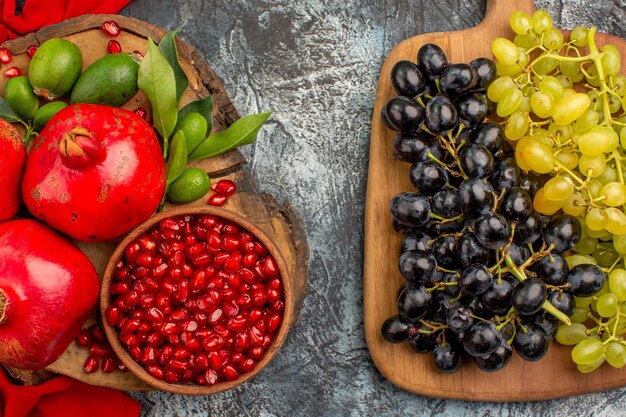 Top close-up view fruits bunches of grapes on the board pomegranates on the red tablecloth