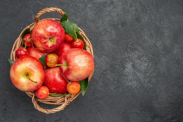 Top close-up view fruits cherries and apples in the basket on the dark table