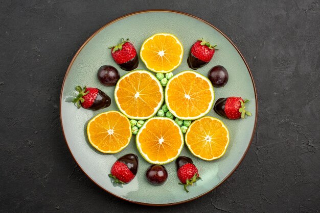 Top close-up view fruits and chocolate chopped orange with chocolate-covered strawberries and green candies