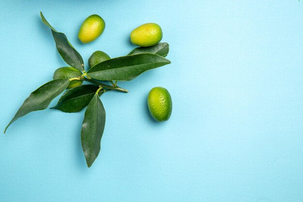 Top close-up view fruits green citrus fruits with leaves on the blue table