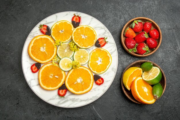 Top close-up view fruits on table white plate of orange chocolate-covered strawberries and lemon and brown bowls of citrus fruits and berries on the table