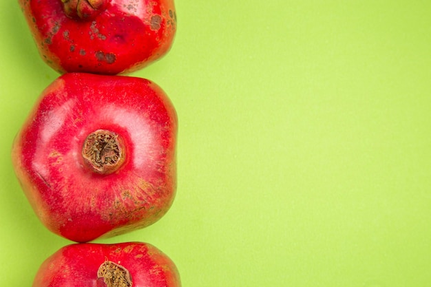 Free photo top close-up view fruits three red pomegranates on the left side of the green table