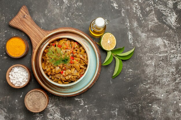 Top close-up view green beans with tomatoes tomatoes and green beans in the plate and three kinds of spices next to the bottle of oil lemon and leaves