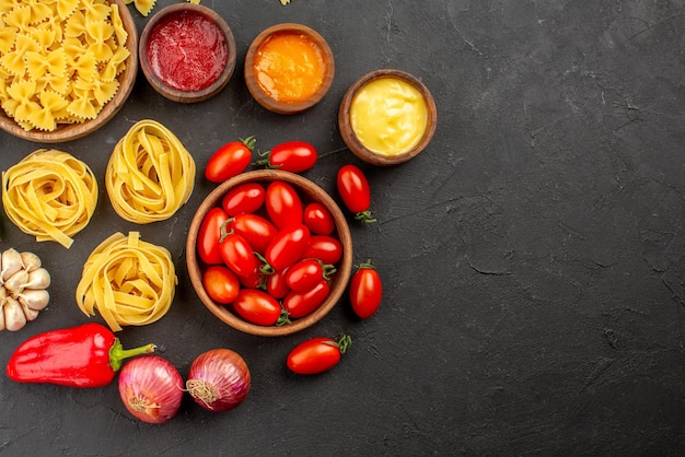 Free photo top close-up view pasta and tomatoes bowls of pasta and tomatoes onion garlic three kind of sauces on the table