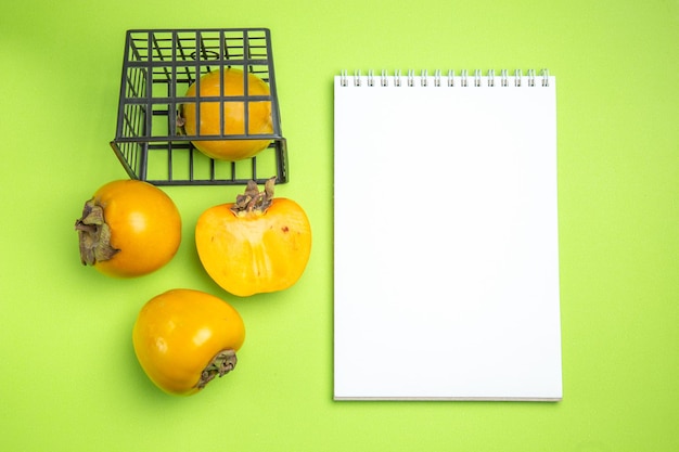 Free photo top close-up view persimmons three persimmons next to the persimmon in the grey basket notebook