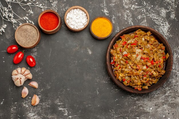 Free Photo top close-up view plate of beans green beans tomatoes next to the bowls of colorful spices and garlic on the dark table