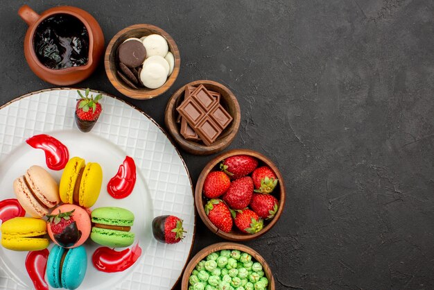 Top close-up view plate of sweets chocolate-covered strawberries French macaroons in the plate five bowls of sweets on the table