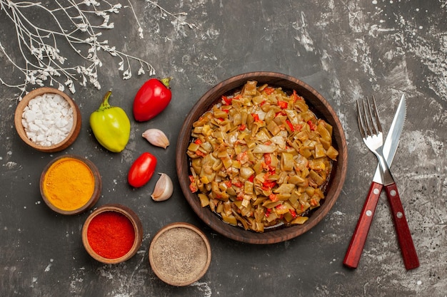 Free photo top close-up view plate on the table appetizing dish of green beans next to the bowls of colorful spices tomatoes garlic ball pepper fork and knife on the dark table