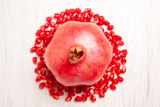 Free photo top close-up view pomegranate red ripe pomegranate next to the seeds of the pomegranate on the white table