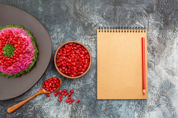 Top close-up view pomegranates an appetizing dish bowl of pomegranate seeds notebook pencil