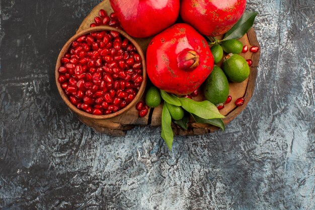 Top close-up view pomegranates pomegranate seeds in bowl three pomegranates on the cutting board