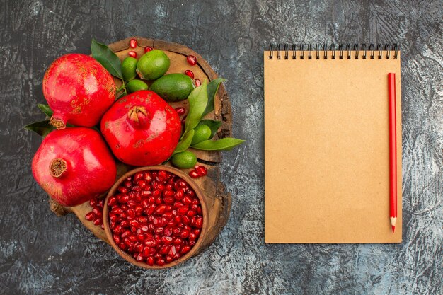 Top close-up view pomegranates pomegranates on the wooden board cream notebook red pencil