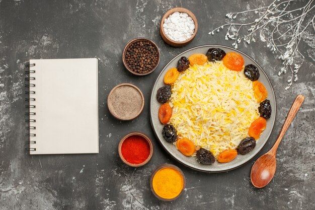 Free photo top close-up view rice rice with dried fruits in the plate five bowls of spices white notebook