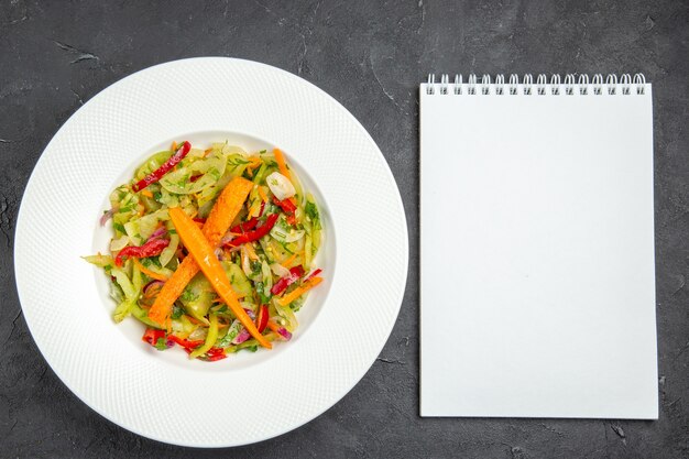 Top close-up view salad plate of an appetizing salad with carrots bell peppers white notebook