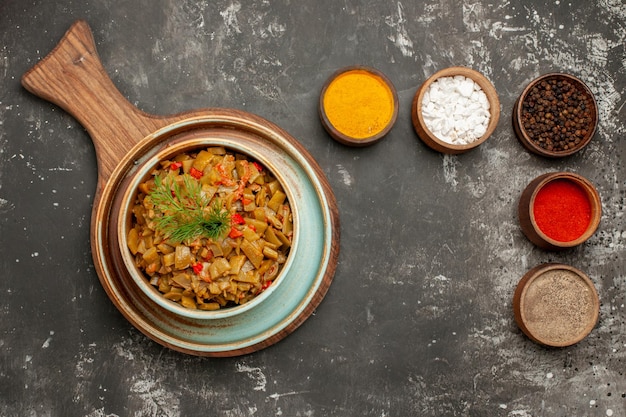 Free Photo top close-up view spices and dish bowls of different spices next to the dish of green beans and tomatoes on the wooden tray on the black table