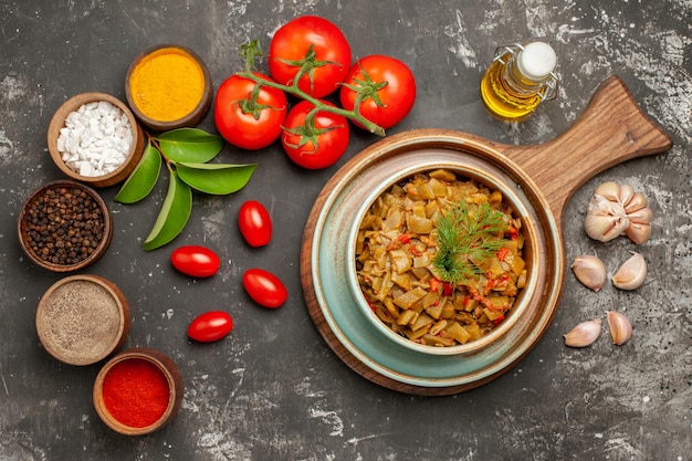 Top close-up view spices plate of green beans garlic bowls of colorful spices leaves tomatoes with pedicels bottle of oil on the dark table