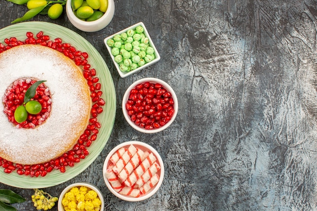 Top close-up view sweets an appetizing cake with seeds of pomegranates citrus fruits and candies