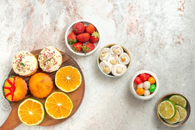 Top close-up view sweets in bowls four bowls of sweets Turkish delight and sliced lime and the wooden cutting board with cookies and orange on the table