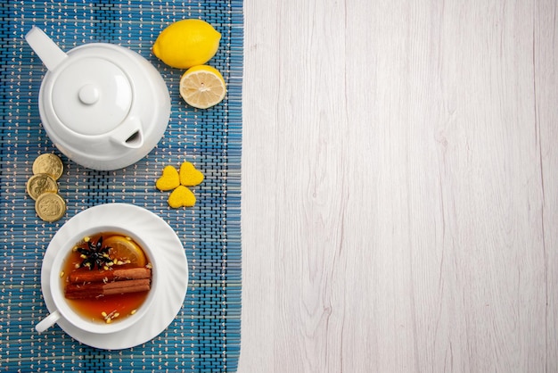 Free photo top close-up view sweets and a cup of tea a cup of herbal tea with lemon and cinnamon lemon teapot different sweets on the checkered tablecloth on the left side of the table