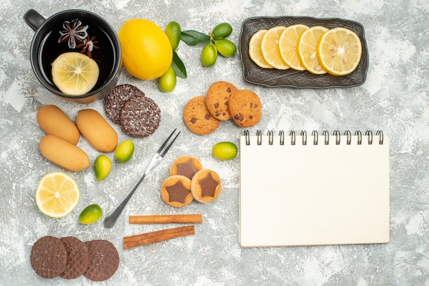 Top close-up view sweets fork the appetizing cookies a cup of tea citrus fruits notebook