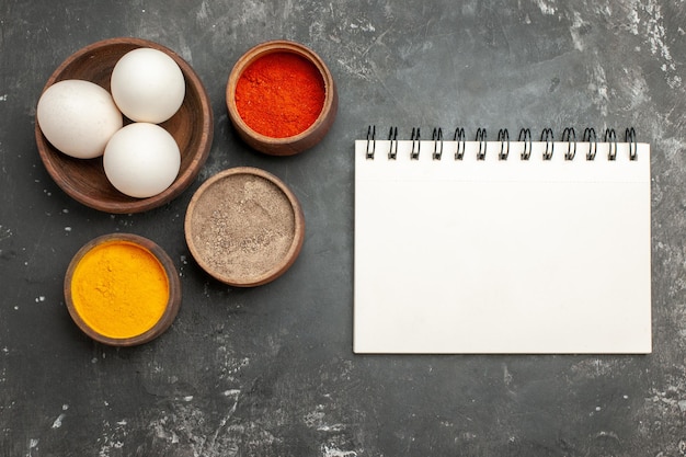 Free photo top close view of bowl of eggs notepad and herbs on dark grey table