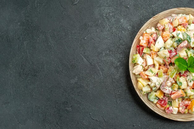 Top close view of bowl of vegetable salad on the right side with green on it on dark green background