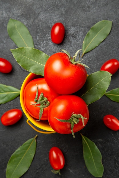 Top close view a bucket with tomatoes around cherry tomatoes and bay leaves on dark ground